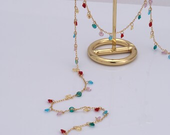 May include: A gold chain necklace with colorful glass beads. The beads are in the shape of hearts and circles. The necklace is displayed on a gold stand.