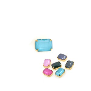 May include: Assortment of colorful glass rhinestones with gold settings. The rhinestones are in various shades of blue, pink, and green.