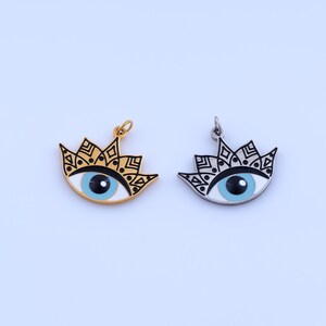 May include: Two eye-shaped pendants. One is gold-colored, the other silver. Both feature a light blue iris, black pupil, and white background. The pendants have a decorative black and gold or silver crown design.
