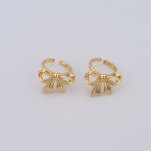 May include: Two gold-toned adjustable rings with a bow design.