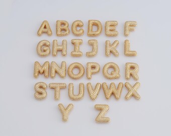 May include: Gold-toned alphabet letter charms with a sparkly finish. Each letter is individually crafted and features a raised design.