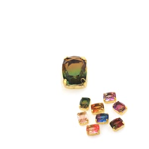 May include: Assortment of colorful, faceted, square-shaped glass gems with gold settings. The gems are arranged in a cluster on a white background.