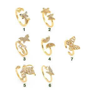 May include: Set of 7 gold-tone rings with clear crystal accents. The rings feature different designs, including butterflies, flowers, and leaves.