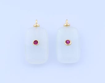 Puede incluir: Dos colgantes rectangulares de piedra blanca, cada uno con una pequeña gema roja redonda en el centro. Tienen lazos dorados en la parte superior. El fondo es azul claro.
