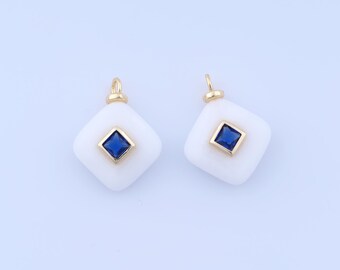 May include: Two white, square pendants with a gold border and a square, dark blue gemstone in the centre. Each pendant has a small gold loop at the top for hanging. The background is a light blue.