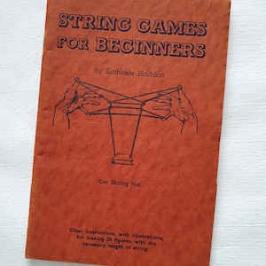 May include: A vintage softcover book titled String Games for Beginners by Kathleen Haddon with a burnt orange cover. The front features a black line drawing of hands creating a string figure and text stating One Shilling Net and instructions.