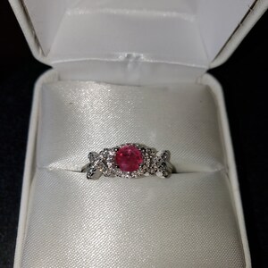 May include: A ring with a pink gemstone surrounded by smaller clear gemstones. The ring is in a white ring box.