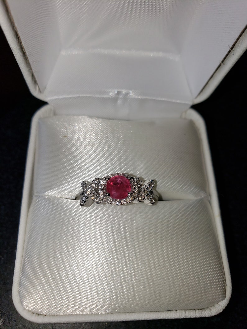 May include: A ring with a pink gemstone surrounded by smaller clear gemstones. The ring is in a white ring box.