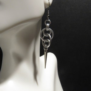 May include: Silver earrings with a chain link design and a pointed drop. The earrings are on a white mannequin head.