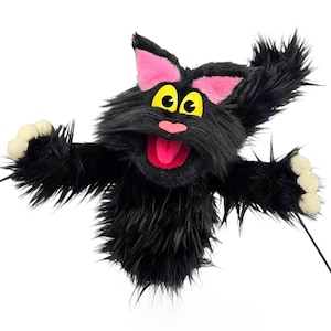 Peut inclure: Marionnette de chat noir avec des yeux jaunes, des oreilles roses et une langue rose. La marionnette a une apparence duveteuse et hirsute et des bras tendus avec des coussinets blancs. Un fil noir est attaché à la marionnette.