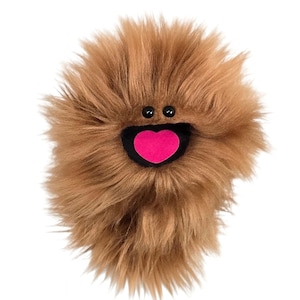 May include: A round, brown, shaggy plush toy with long, soft faux fur. The creature features two small, round, black plastic eyes positioned above a wide, black, open mouth containing a bright pink, heart-shaped tongue centered inside.