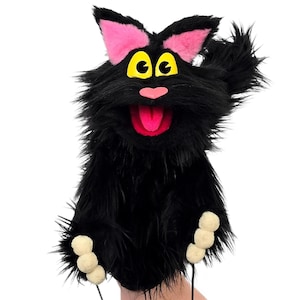 May include: A black cat hand puppet with a fluffy texture. The puppet has pink ears, yellow eyes, and a pink nose and tongue. The puppet's paws are made of three beige pom-poms. The puppet is designed to be worn on the hand.