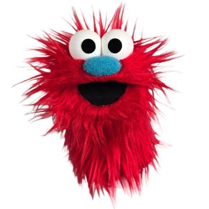 May include: A red fuzzy hand puppet featuring long synthetic fur, two large white spherical eyes with black pupils, and a bright blue textured nose. The puppet has an open mouth with a black interior, creating a distinct character appearance.