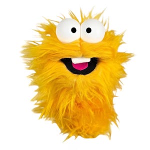 May include: A bright yellow fuzzy puppet with long, shaggy synthetic fur. It features two large, round white eyes with black pupils, a wide open mouth with a black interior, a single white tooth, and a small pink tongue visible inside.