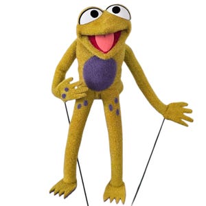 Puede incluir: Títere de rana amarilla con vientre morado y ojos blancos grandes. La rana tiene una lengua roja y posa con los brazos y las piernas extendidos. Cuerdas negras adjuntas para la manipulación.