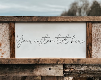 Op de afbeelding: Een rechthoekig houten bord met een rustiek frame. Het bord heeft een wit middenpaneel met de tekst "Your custom text here" in zwart schrift. De zijkanten hebben panelen met een koeienhuidpatroon.