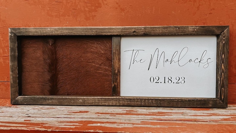 Op de afbeelding: Een houten ingelijst bord met een bruine lederen achtergrond en een wit canvas paneel met de tekst "The Mahlocks 02.18.23" in zwarte cursieve letters.