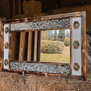May include: A rustic wooden mirror with a cowhide frame and turquoise accents. The mirror has a Southwestern design with geometric patterns.