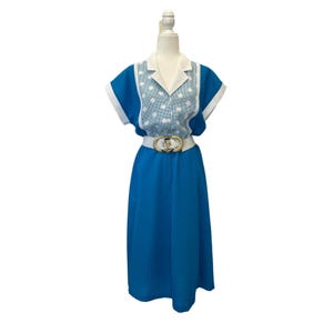 May include: A blue and white polka dot dress with a white collar and short sleeves. The dress has a white belt with a gold buckle.