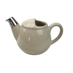 Könnte beinhalten: Ein cremefarbener Keramik-Milchkännchen mit einem silbernen Deckel und einem Ausguss. Der Milchkännchen hat einen abgerundeten Körper und einen Griff.