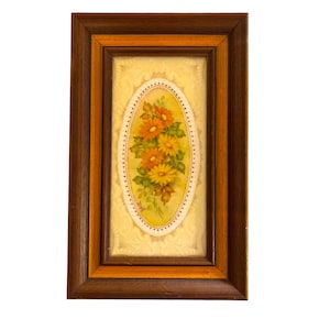 Può includere: Un dipinto incorniciato di un bouquet di fiori gialli e arancioni con foglie verdi. I fiori sono dipinti in una forma ovale su uno sfondo crema con un bordo dorato.