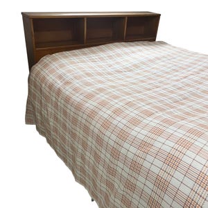 May include: A wooden headboard with three storage compartments above a bed covered with a cream-colored plaid blanket. The plaid pattern features thin lines of brown and orange.