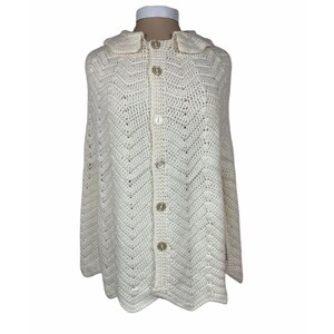 May include: A white crocheted hooded poncho with a button fastening down the front.