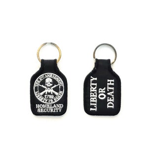 May include: Two black leather keychains with silver embroidery. One keychain features a skull and crossbones with the text "The 2nd Amendment 1789 Liberty or Death" and "Homeland Security". The other keychain features the text "Liberty or Death".