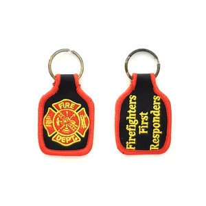 May include: Two black keychains with red trim. One keychain features a gold embroidered firefighter emblem with the words "Fire Dept." The other keychain has the words "Firefighters First Responders" embroidered in gold.