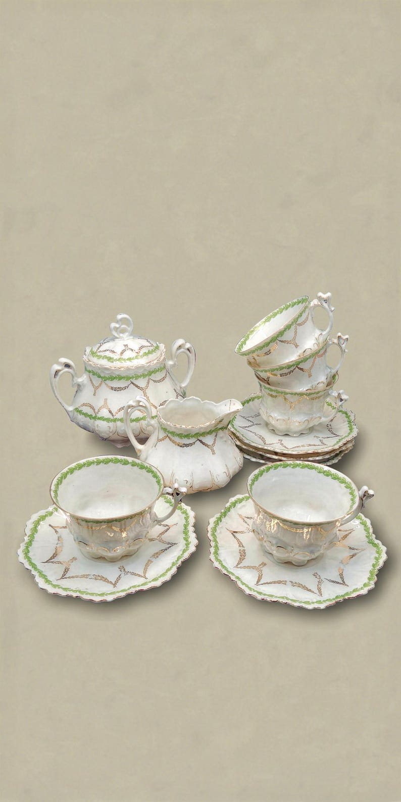 May include: A white porcelain tea set with gold trim and green accents. The set includes a teapot, creamer, sugar bowl, and several teacups and saucers. The edges of the cups and saucers have a green scalloped design.