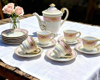 May include: A vintage tea set with a teapot, six teacups, and saucers. The set features a cream and pink color scheme with gold accents. A small vase of pink roses sits nearby. The set is arranged on a white tablecloth.