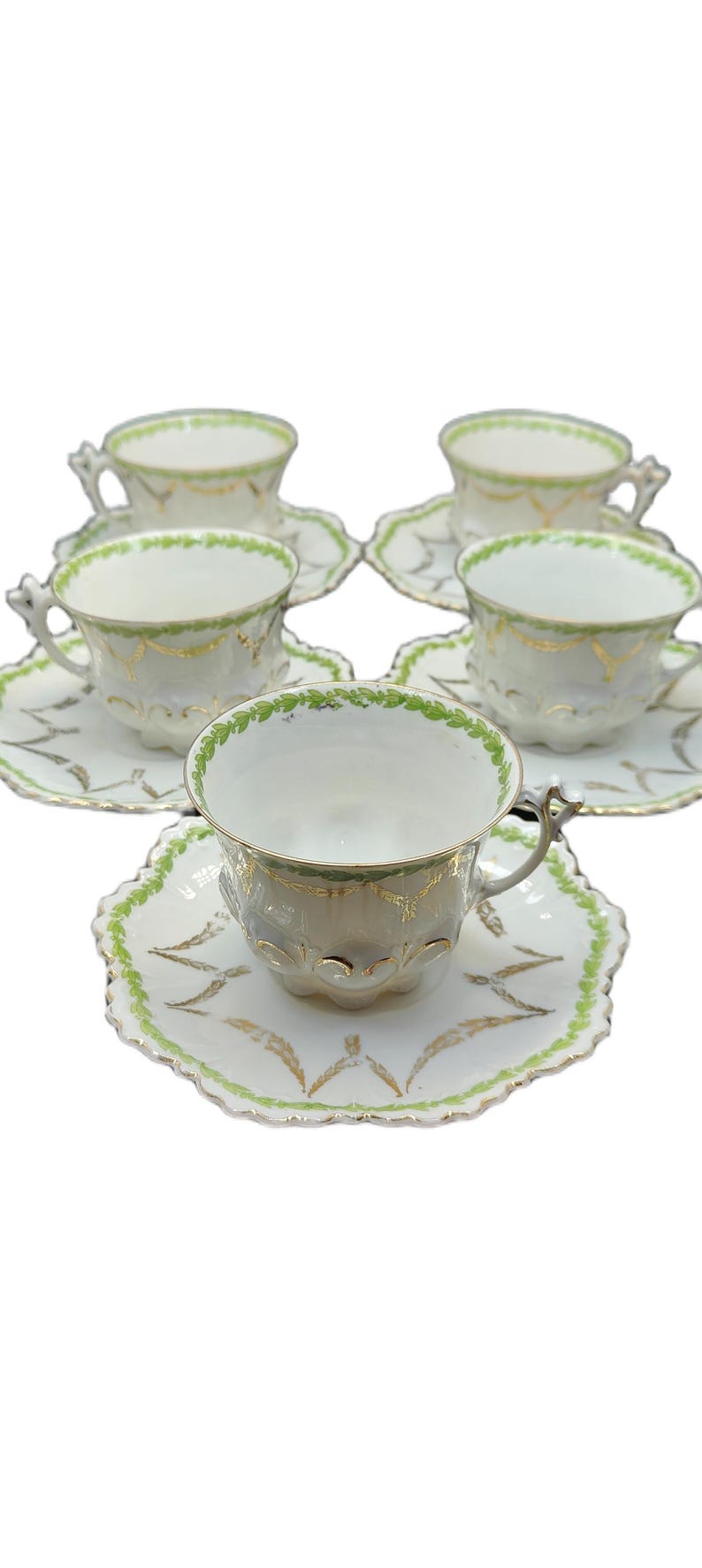 May include: Set of six white teacups and saucers with green and gold leaf design. The teacups have ornate handles and the saucers have a scalloped edge. The teacups and saucers are arranged on a white background.