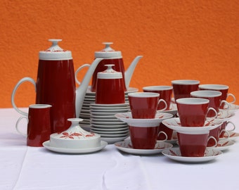 May include: A red and white porcelain tea set with a teapot, creamer, sugar bowl, and cups and saucers. The set features a floral design.