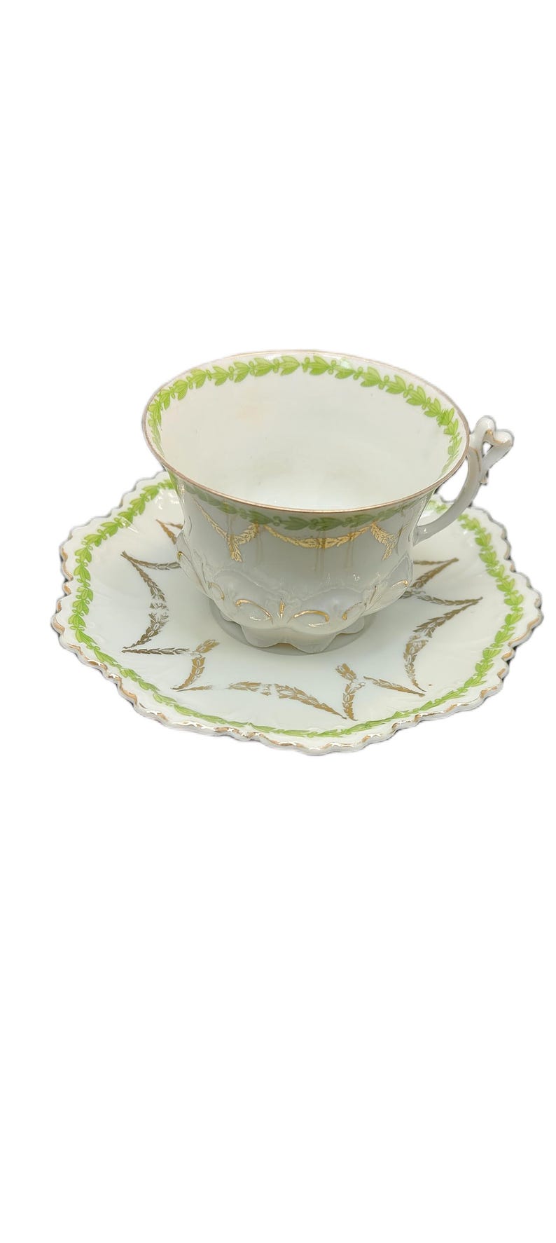 May include: A vintage teacup and saucer set. The cup and saucer are white with gold accents and a green leaf design around the rim and edges. The cup has a decorative handle.