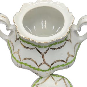 May include: White porcelain sugar bowl with lid. The bowl has a scalloped rim and two handles. It is decorated with gold and green leaf and vine patterns. The lid has a small handle and matching design.