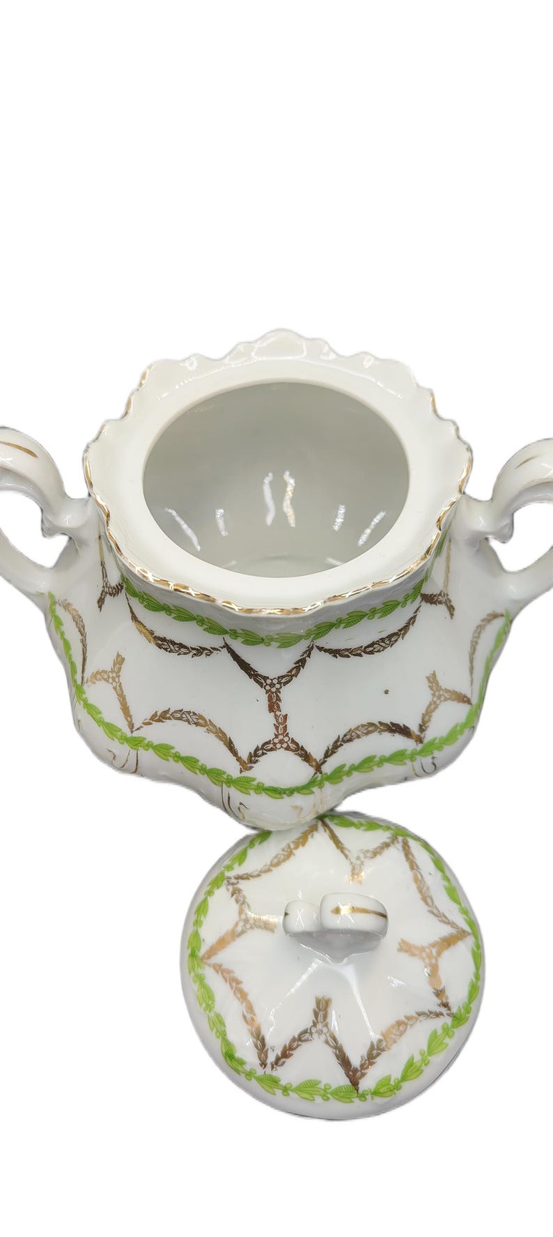 May include: White porcelain sugar bowl with lid. The bowl has a scalloped rim and two handles. It is decorated with gold and green leaf and vine patterns. The lid has a small handle and matching design.