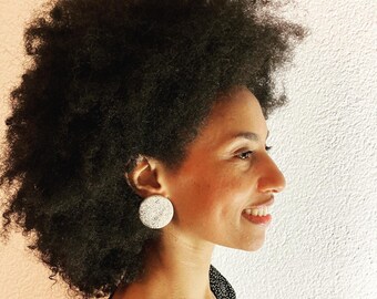 Könnte beinhalten: Eine Frau mit einer großen Afrofrisur trägt einen runden Ohrring mit weißen und schwarzen Flecken. Der Ohrring ist an ihrem linken Ohr sichtbar.
