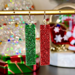 May include: A pair of dangle earrings with silver hooks. The earrings are rectangular and feature green and red glitter.