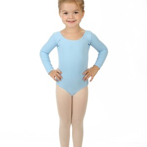 May include: A young girl wearing a light blue long-sleeved leotard and pink ballet shoes. She has her hair pulled back in a bun.
