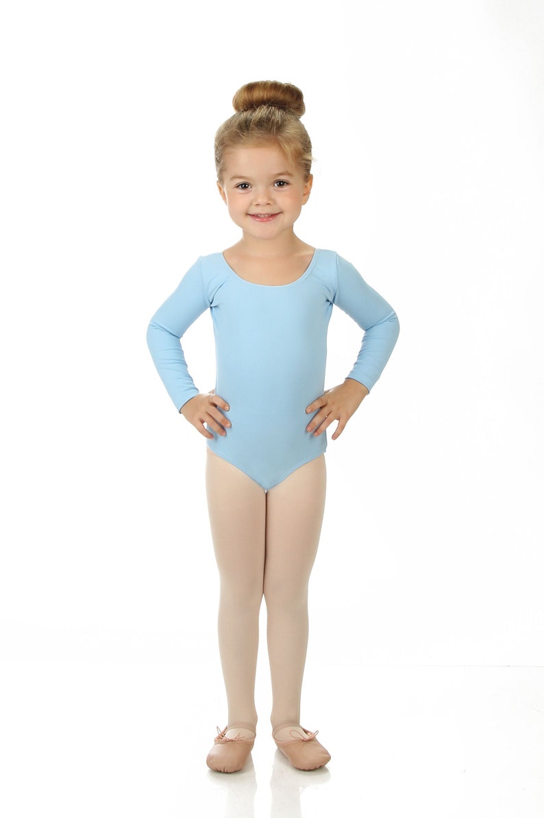 May include: A young girl wearing a light blue long-sleeved leotard and pink ballet shoes. She has her hair pulled back in a bun.