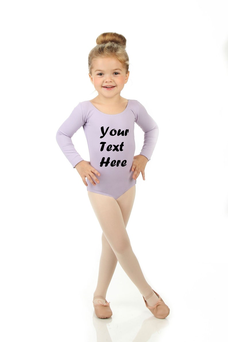 May include: A young girl wearing a lavender leotard with long sleeves and the text "Your Text Here" printed on the front. She is wearing pink ballet shoes and has her hair pulled back in a bun.