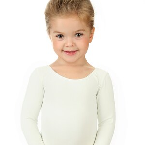 May include: A young girl with blonde hair in a bun is wearing a white long-sleeved leotard. She is smiling and looking at the camera.