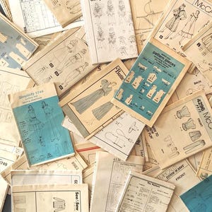 May include: A collection of vintage sewing patterns scattered in an overlapping arrangement. The paper envelopes feature black and white line drawings of clothing designs, technical diagrams, and blue accents with printed brand names like Simplicity.