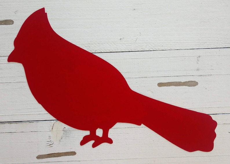 May include: A red cardinal silhouette cut out of paper or metal. The cardinal is facing right and has a long tail.