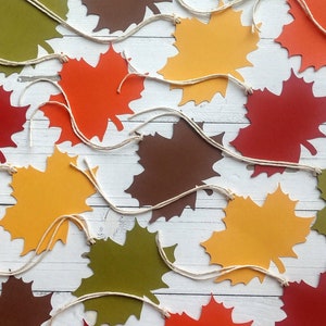 May include: A garland of paper maple leaves in various fall colors, including red, orange, yellow, brown, and green, with white twine strung between each leaf.