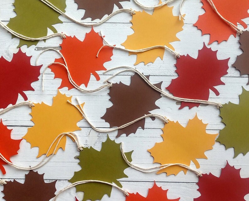 May include: A garland of paper maple leaves in various fall colors, including red, orange, yellow, brown, and green, with white twine strung between each leaf.