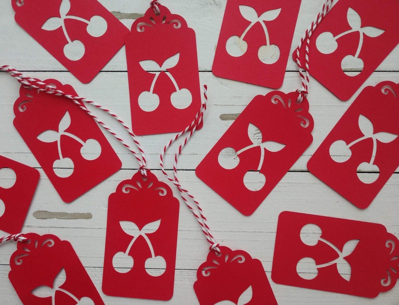May include: Red gift tags with white cherry silhouettes. The tags have a scalloped edge and are tied with twine.