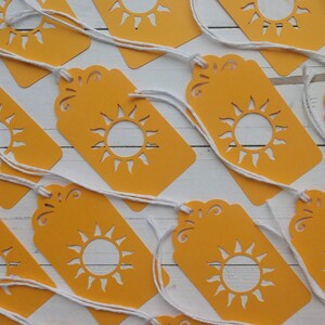 May include: A set of ten yellow gift tags with a white sun cut-out design. Each tag has a white string attached.