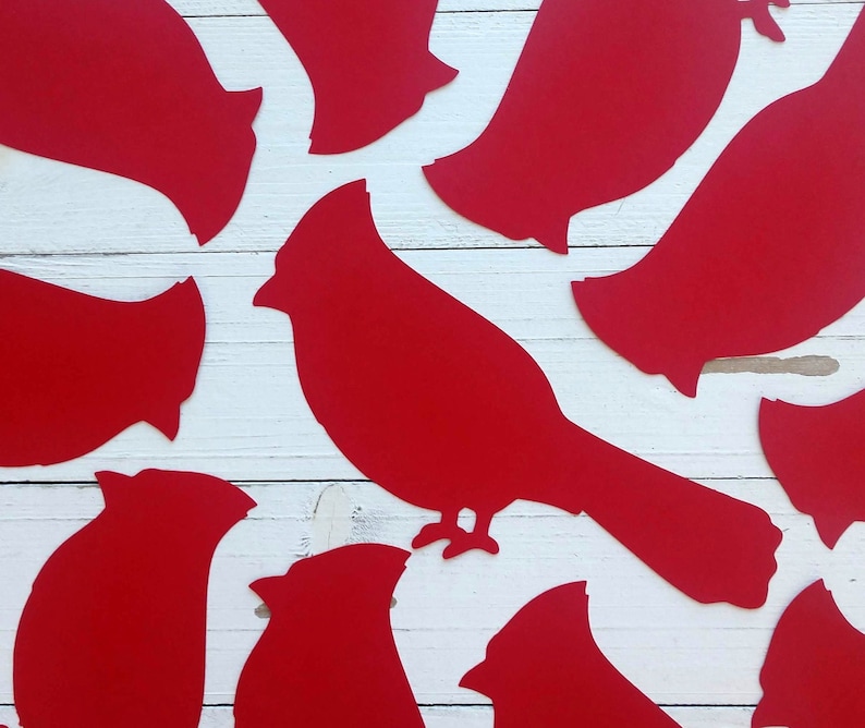 May include: Red paper cutouts of cardinal birds in various sizes and poses on a white wooden background.