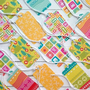 May include: Assortment of colourful gift tags with various travel-themed patterns, including aeroplanes, stars, arrows, and cars. The tags are tied with white string.